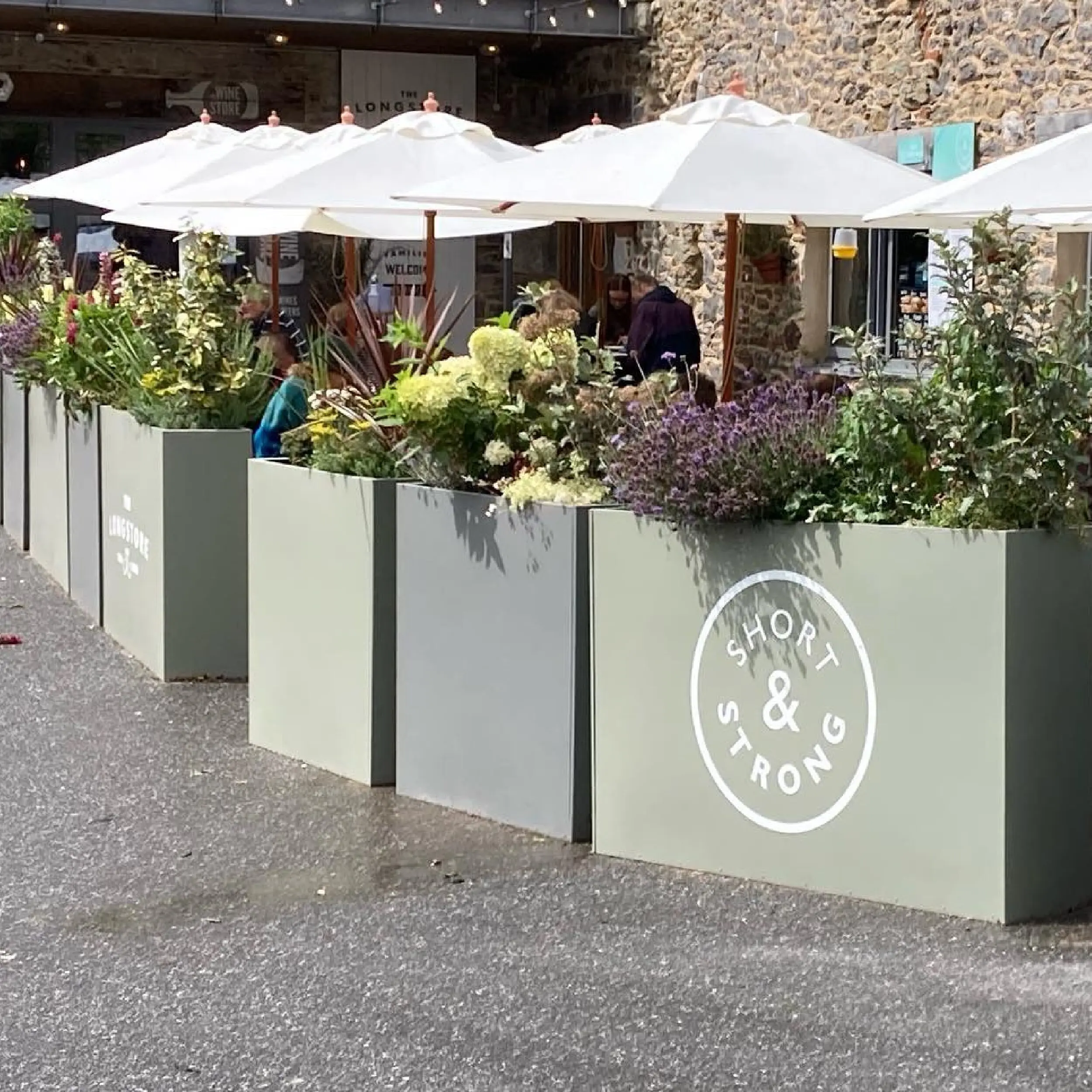 Strong & Short 1 - Forjado Powder Coated Café Planter Short & Strong in Cornwall Forjado Metal Planters Powder Coated in Green with their logos to all, Commercial Planters, Heavy Duty Cafe Planters, Metal Planters, Bespoke Cafe Planters, Branded Cafe Planters, Custom Cafe Planters, Outdoor Cafe Planters, Pavement Planters