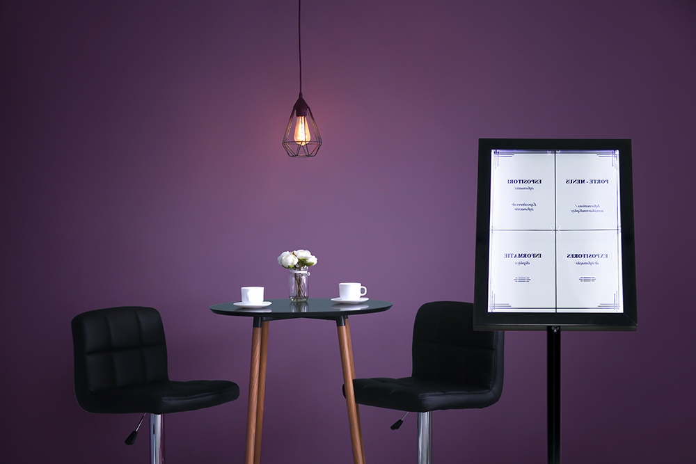 Seren XL Black LED Menu Display Stand next to a table and chairs set inside Seren XL Black LED Menu Display Stand next to a table and chairs set inside, Menu Stands, Menu Display Stands, LED Menu Stands, Freestanding Menu Stands, Outdoor Menu Stands, Cafe Menu Stands, Restaurant Menu Stands
