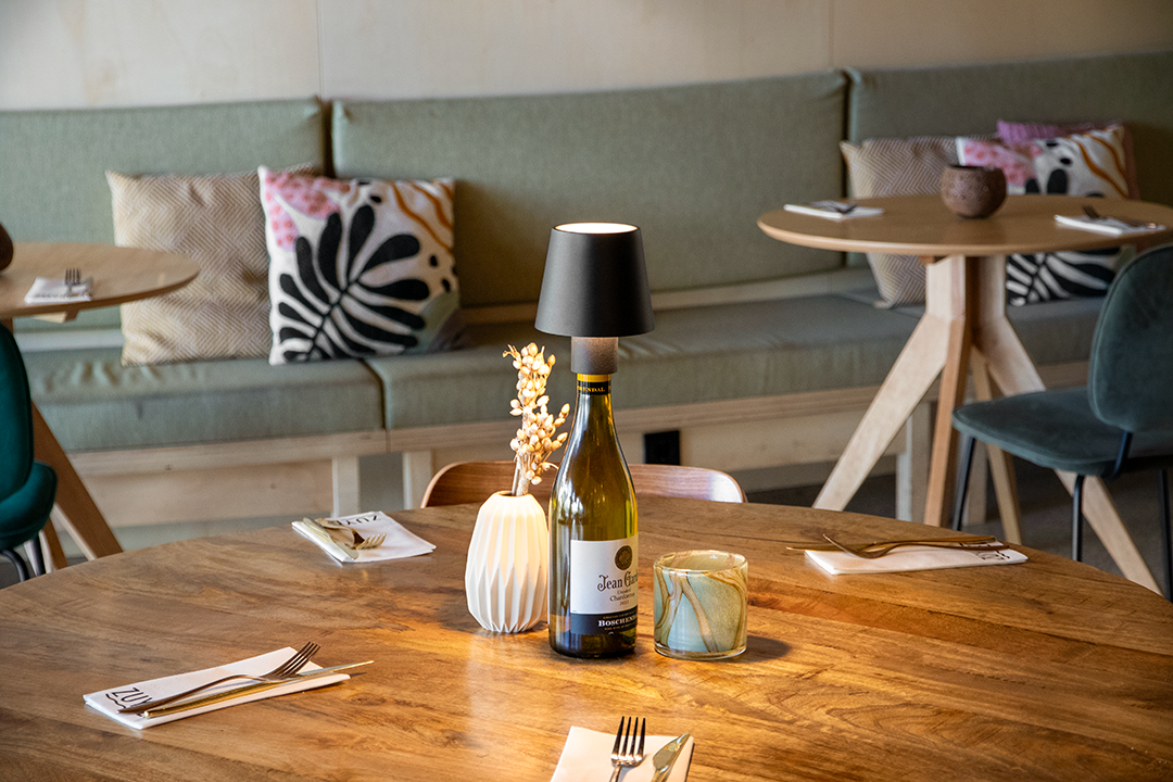 Versailles Rechargeable Bottle Lamp on a Wooden Table Inside a Restaurant Lit Up Versailles Rechargeable Bottle Lamp in Black on a Wooden Table Inside a Restaurant Lit Up, Table Lighting, Restaurant Lighting, Lighting for Table at Restaurant, Commercial Table Lighting, Hospitality Lighting, Rechargeable Bottle Lamps, LED Lighting, Outdoor Bottle Lamps, Indoor Table Lighting, Cafe Lighting, Bottle Lamps for Cafes