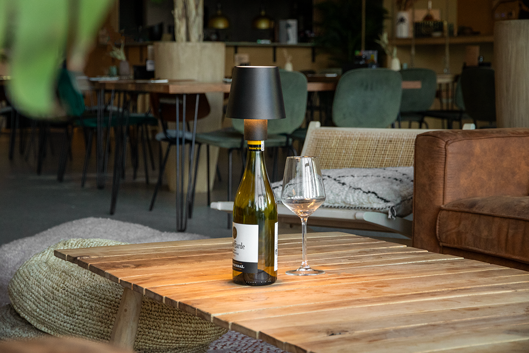 Versailles Rechargeable Bottle Lamp on a Wooden Table Inside a Restaurant Lit Up Next a Wine Glass Versailles Rechargeable Bottle Lamp in Black on a Wooden Table Inside a Restaurant Lit Up Next a Wine Glass, Table Lighting, Restaurant Lighting, Lighting for Table at Restaurant, Commercial Table Lighting, Hospitality Lighting, Rechargeable Bottle Lamps, LED Lighting, Outdoor Bottle Lamps, Indoor Table Lighting, Cafe Lighting, Bottle Lamps for Cafes