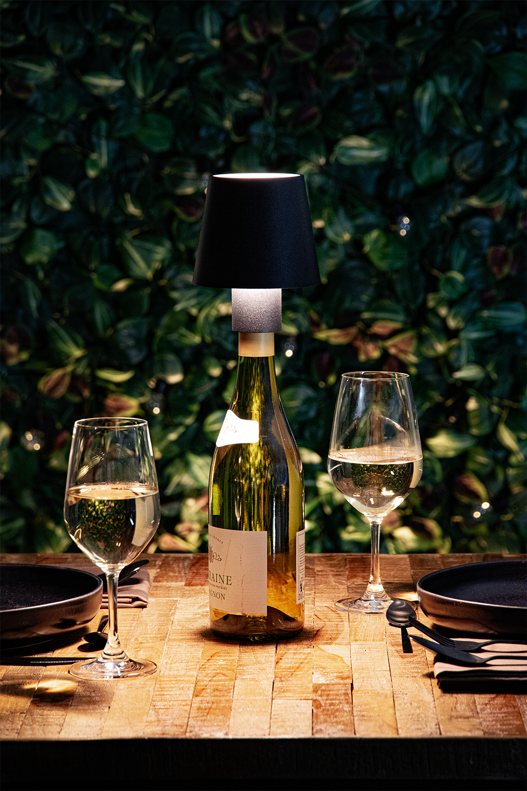 Versailles Rechargeable Bottle Lamp on a Wooden Table Outside a Restaurant Lit Up Next to Wine Glasses at Night-Time Versailles Rechargeable Bottle Lamp in Black on a Wooden Table Outside a Restaurant Lit Up Next to Wine Glasses at Night-Time, Table Lighting, Restaurant Lighting, Lighting for Table at Restaurant, Commercial Table Lighting, Hospitality Lighting, Rechargeable Bottle Lamps, LED Lighting, Outdoor Bottle Lamps, Indoor Table Lighting, Cafe Lighting, Bottle Lamps for Cafes