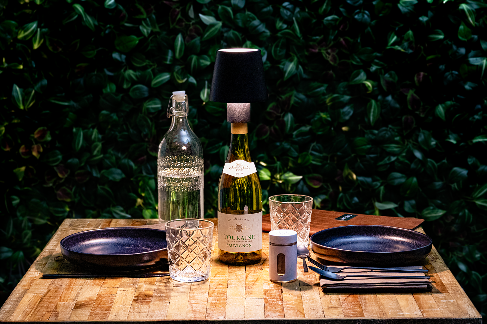 Versailles Rechargeable Bottle Lamp on a Wooden Table Outside a Restaurant Lit Up in a Table Setting at Night-Time Versailles Rechargeable Bottle Lamp in Black on a Wooden Table Outside a Restaurant Lit Up in a Table Setting at Night-Time, Table Lighting, Restaurant Lighting, Lighting for Table at Restaurant, Commercial Table Lighting, Hospitality Lighting, Rechargeable Bottle Lamps, LED Lighting, Outdoor Bottle Lamps, Indoor Table Lighting, Cafe Lighting, Bottle Lamps for Cafes