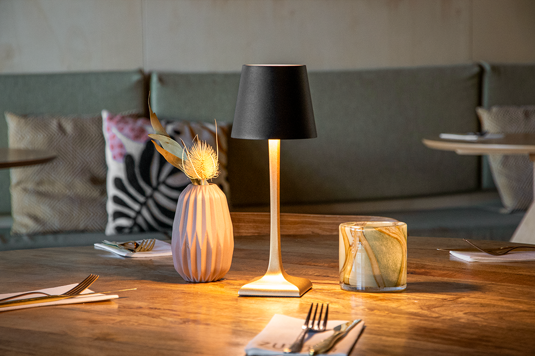 Labaro Rechargeable Table Lamp on a Wooden Table Inside a Restaurant Lit Up Labaro Rechargeable Table Lamp in Black on a Wooden Table Inside a Restaurant Lit Up, Table Lighting, Restaurant Lighting, Lighting for Table at Restaurant, Commercial Table Lighting, Hospitality Lighting, Rechargeable Table Lamps, LED Lighting, Outdoor Table Lamps, Indoor Table Lighting, Cafe Lighting, Table Lamps for Cafes